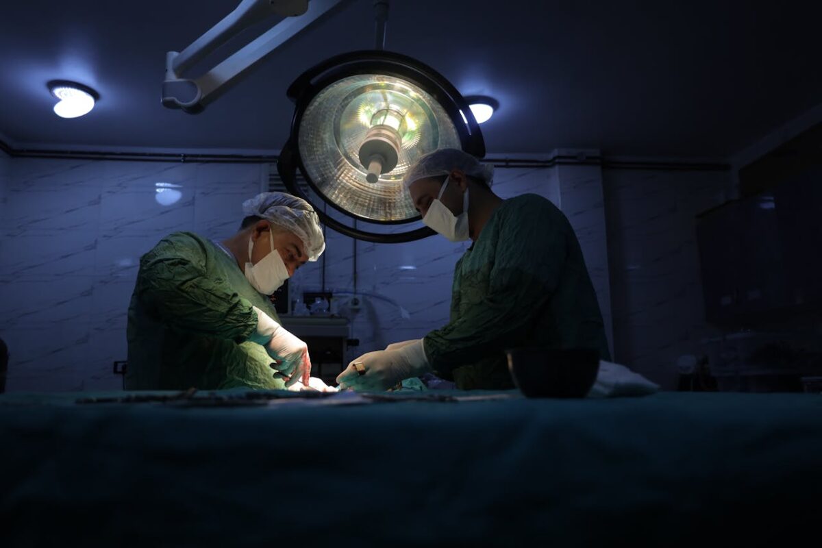 Two surgeons in a dimly lit operating room in Idlib, Syria, perform a surgical procedure.